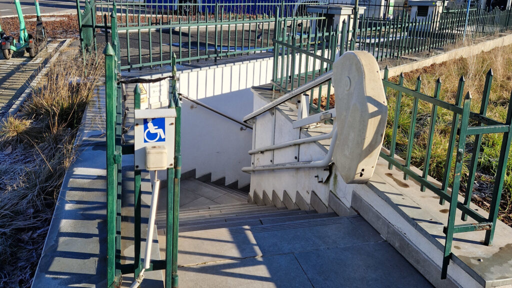Wejście do obiektu wyposażone w platformę schodową dla osób z niepełnosprawnościami. System umożliwia bezpieczne pokonanie schodów osobom na wózku inwalidzkim lub o ograniczonej mobilności. Dodatkowo przy wejściu znajduje się wyraźne oznakowanie informujące o dostępności obiektu dla użytkowników z niepełnosprawnościami.
